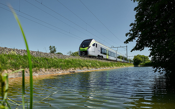 Ein silbriger Zug fährt auf einem Damm am Wasser entlang